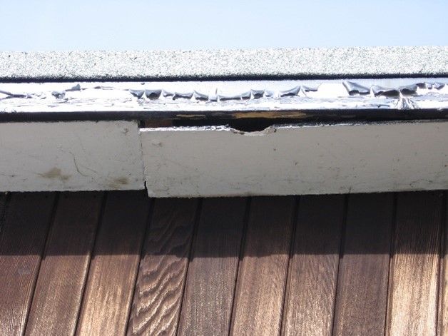 A damaged asbestos insulating board soffit panel pulling away from the roof eaves above timber cladding