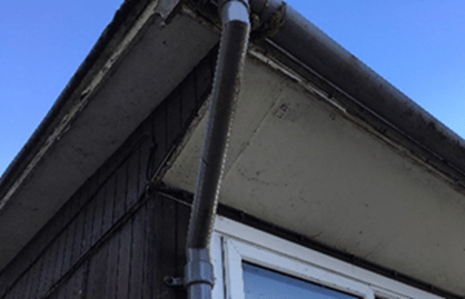 Asbestos insulating board soffit panels under the eaves of a roof, beside a downpipe