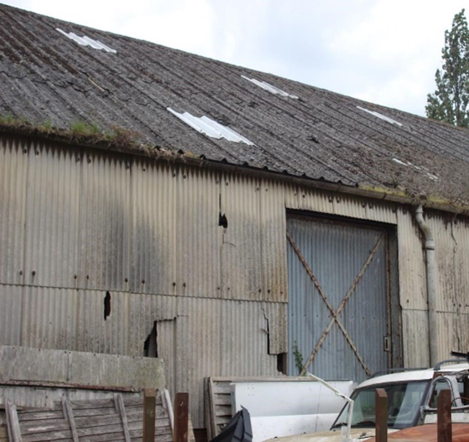 Outbuilding with a weathered corrugated asbestos cement roof, damaged corrugated wall cladding and a cement downpipe