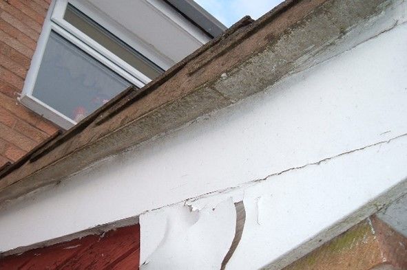 Asbestos cement undercloaking board beneath the overhang at the edge of a house roof, with flaking paint