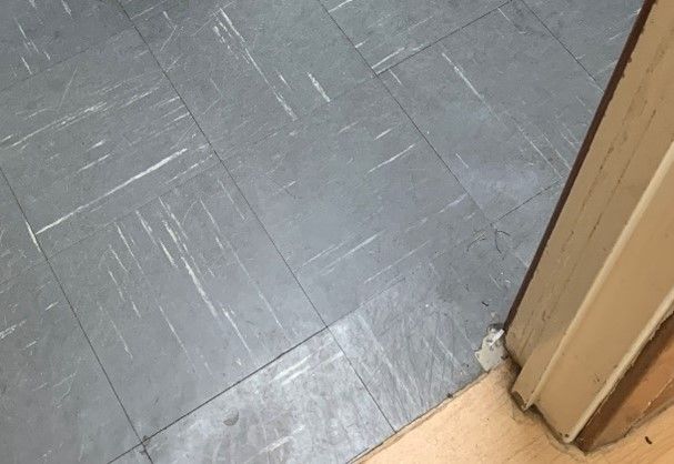 Worn grey vinyl floor tiles with scuff marks, one tile chipped beside a door frame